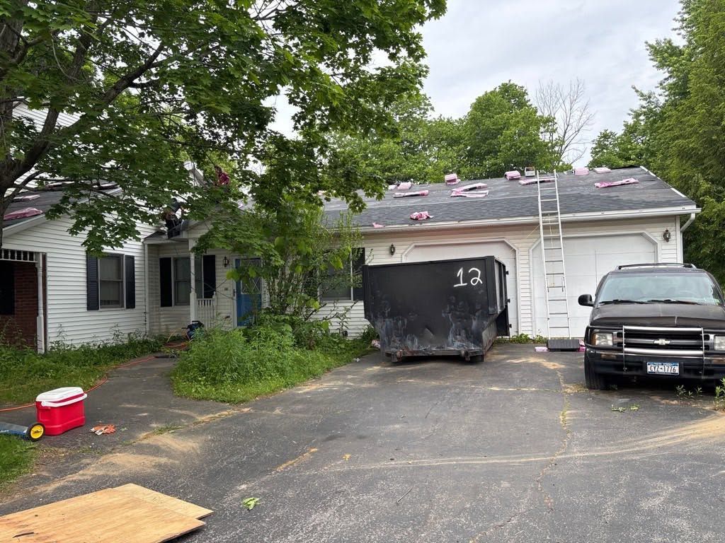 Suburban driveway with a black pickup, tarp-covered trailer, and house under trees