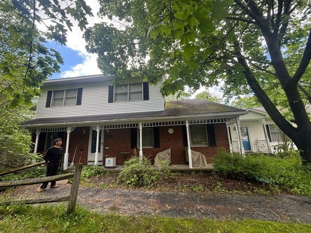 Two-story brick house with white porch and trees, seen from the front on a cloudy day