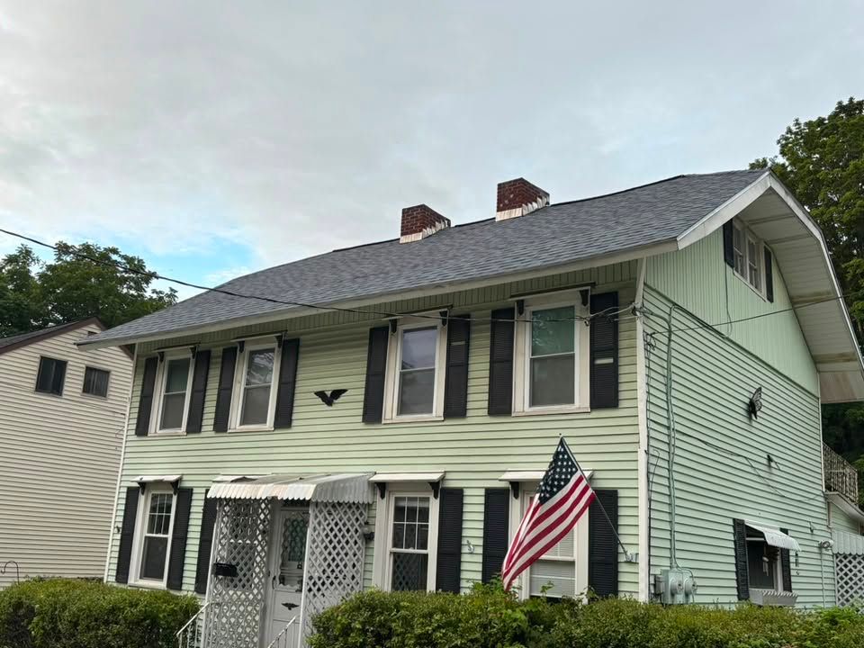 Two-story pale green house with black shutters and an American flag hanging by the front door