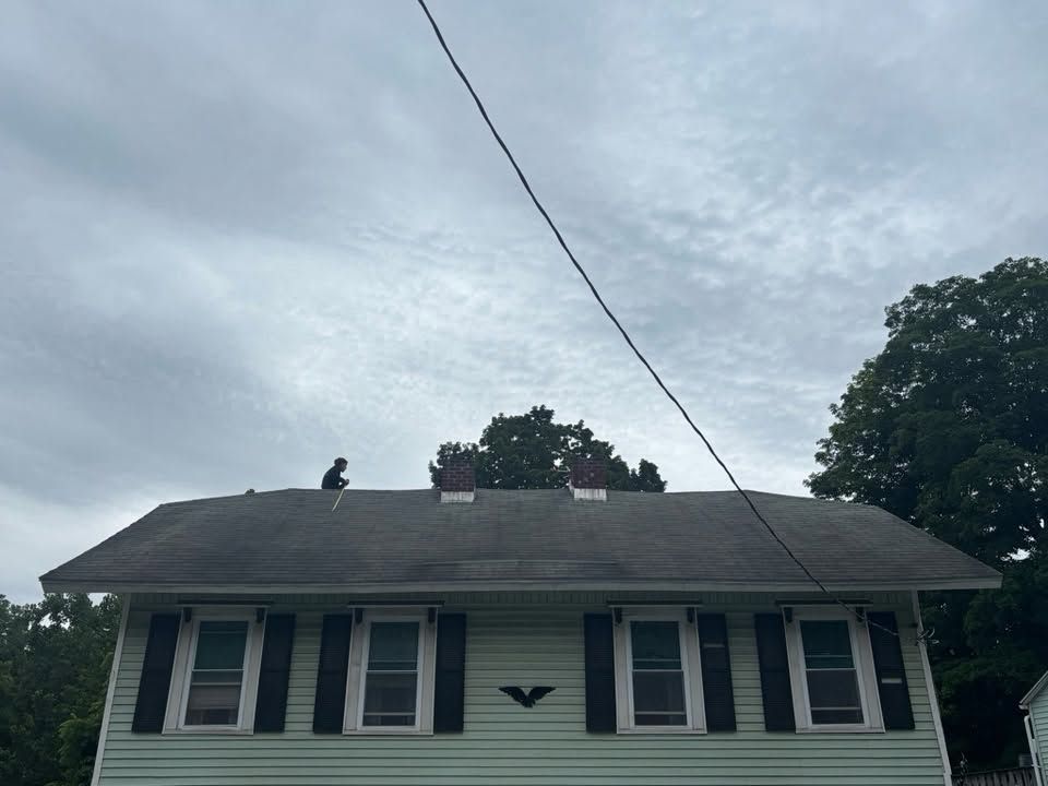 House with gray roof and white siding under a cloudy sky, with trees and a power line overhead
