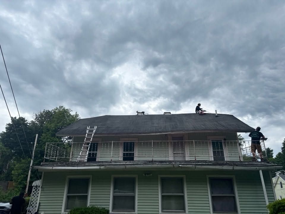 Workers on a roof repairing a two-story green house under a cloudy sky
