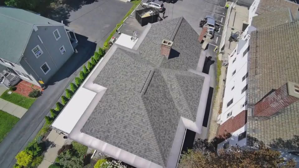 Aerial view of a gray-shingled house with neighboring homes and a street.