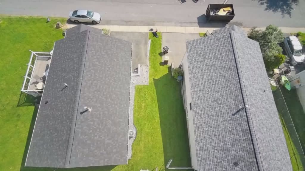 Aerial view of two gray-roof houses with a green yard and parked cars along the street.