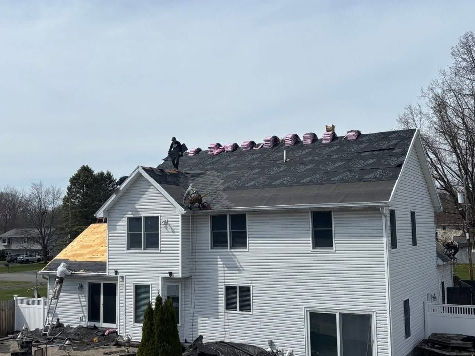 Workers on a house roof installing pink insulation or shingles on a white two-story home