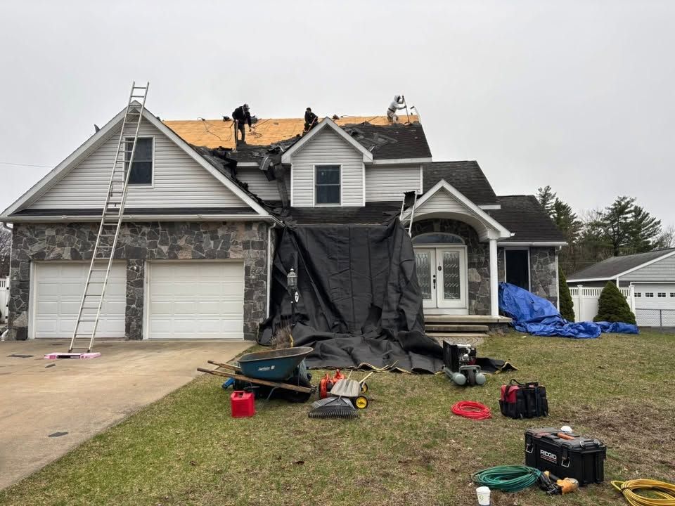 Damaged house roof under repair with ladders, black tarp, and construction tools in the front yard