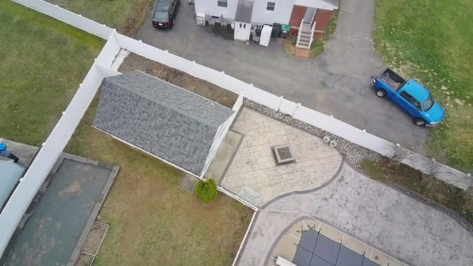 Aerial view of a yard with a white fence, gray-roofed shed, paved driveway, and blue pickup truck.