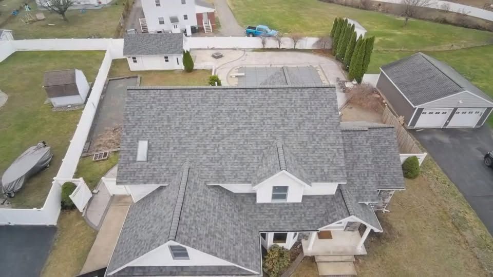 Aerial view of a gray-roofed suburban house with driveway, detached garage, and neighboring homes.