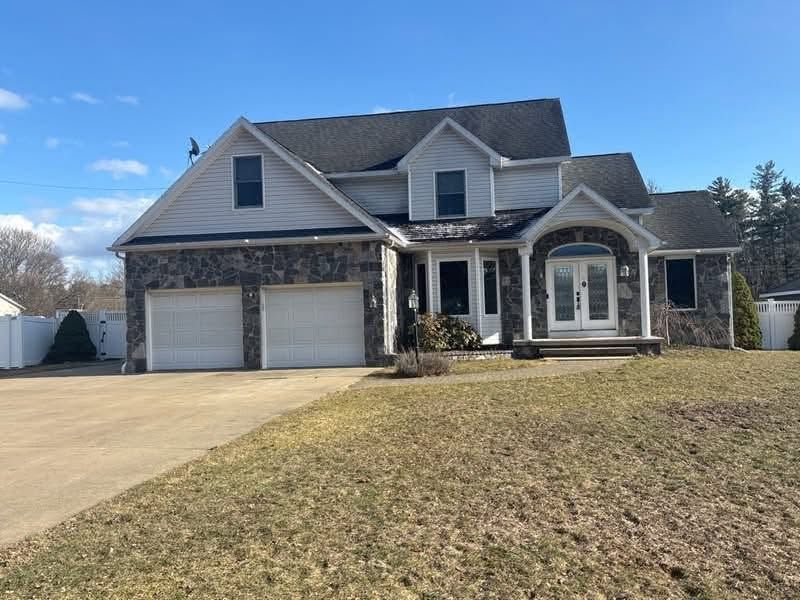 Two-story suburban house with stone front, double garage, and large driveway under a blue sky