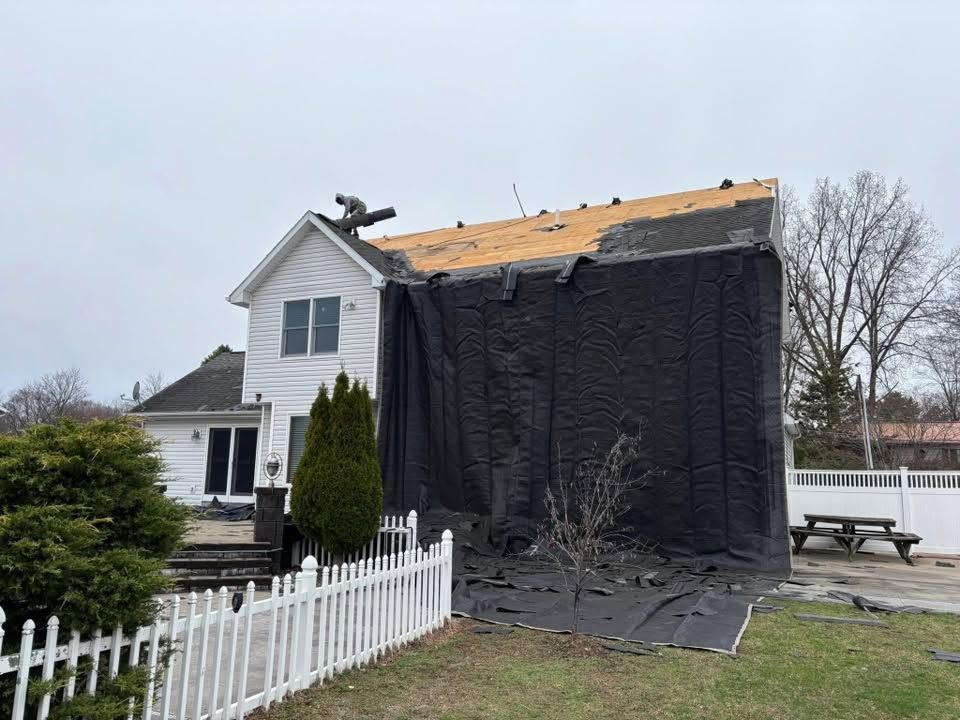 House under repair with large black tarp covering one side and roof work in progress