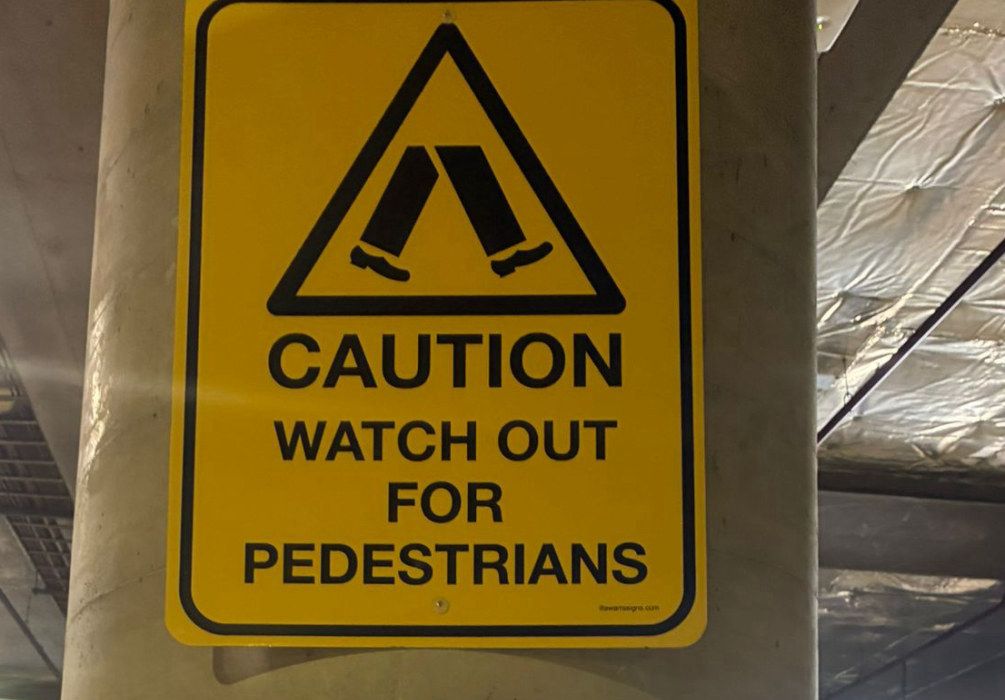 Yellow caution sign: watch out for pedestrians, on a column in a car park