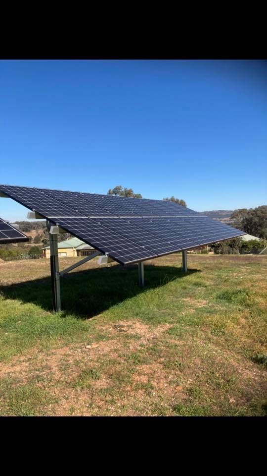 Solar panels on metal supports in a grassy field, blue sky overhead — Todd Basham Electrical in Cootamundra, NSW