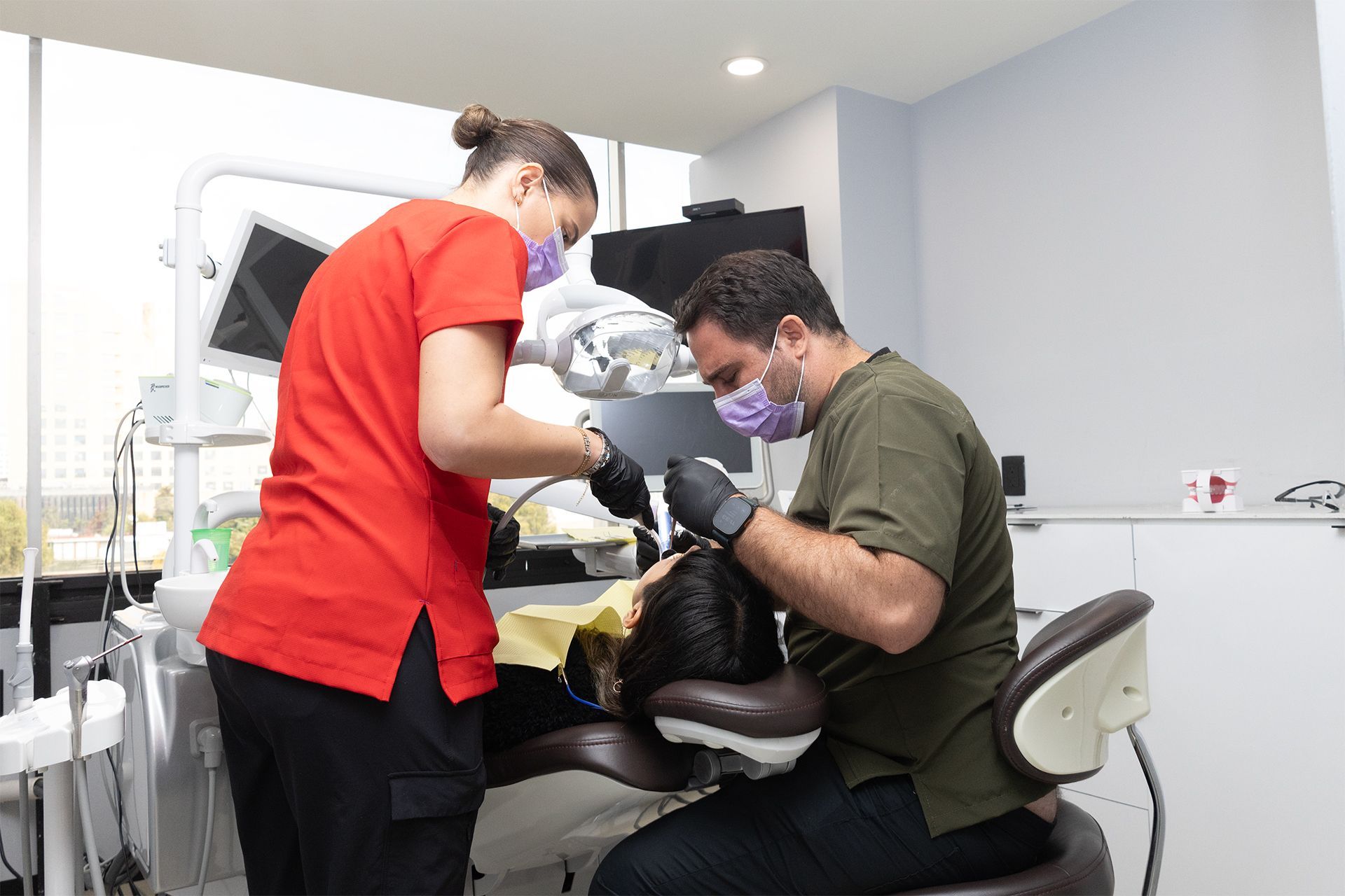 Un hombre y una mujer están trabajando en los dientes de un paciente en un consultorio dental.