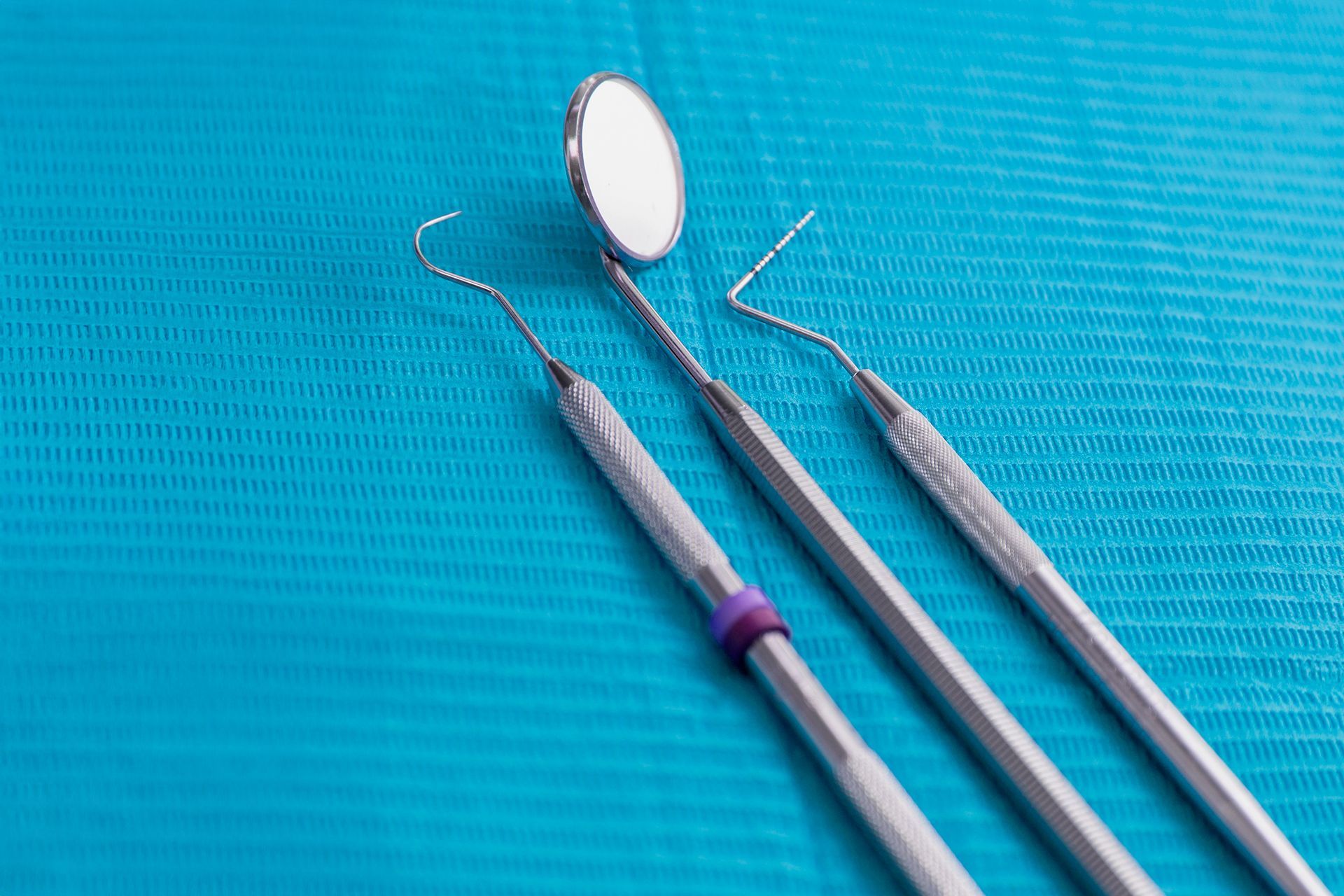 Un primer plano de tres instrumentos dentales sobre una mesa azul.