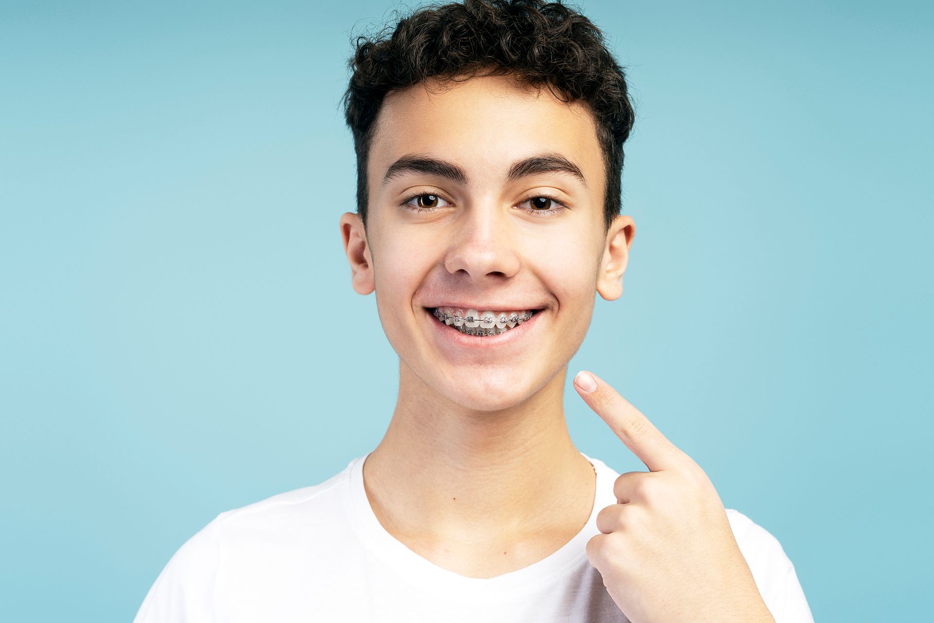 Un joven con aparatos dentales se señala los dientes.