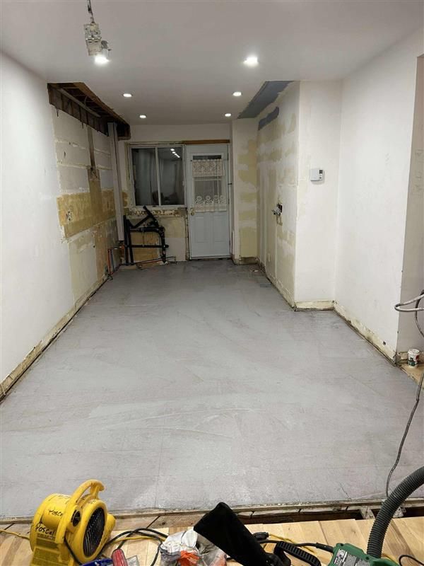 Espace intérieur rénové avec sol gris, murs apparents et porte. Des outils sont visibles au premier plan.