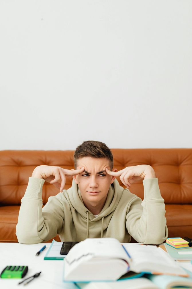 A young man is sitting at a table with his hands on his forehead.