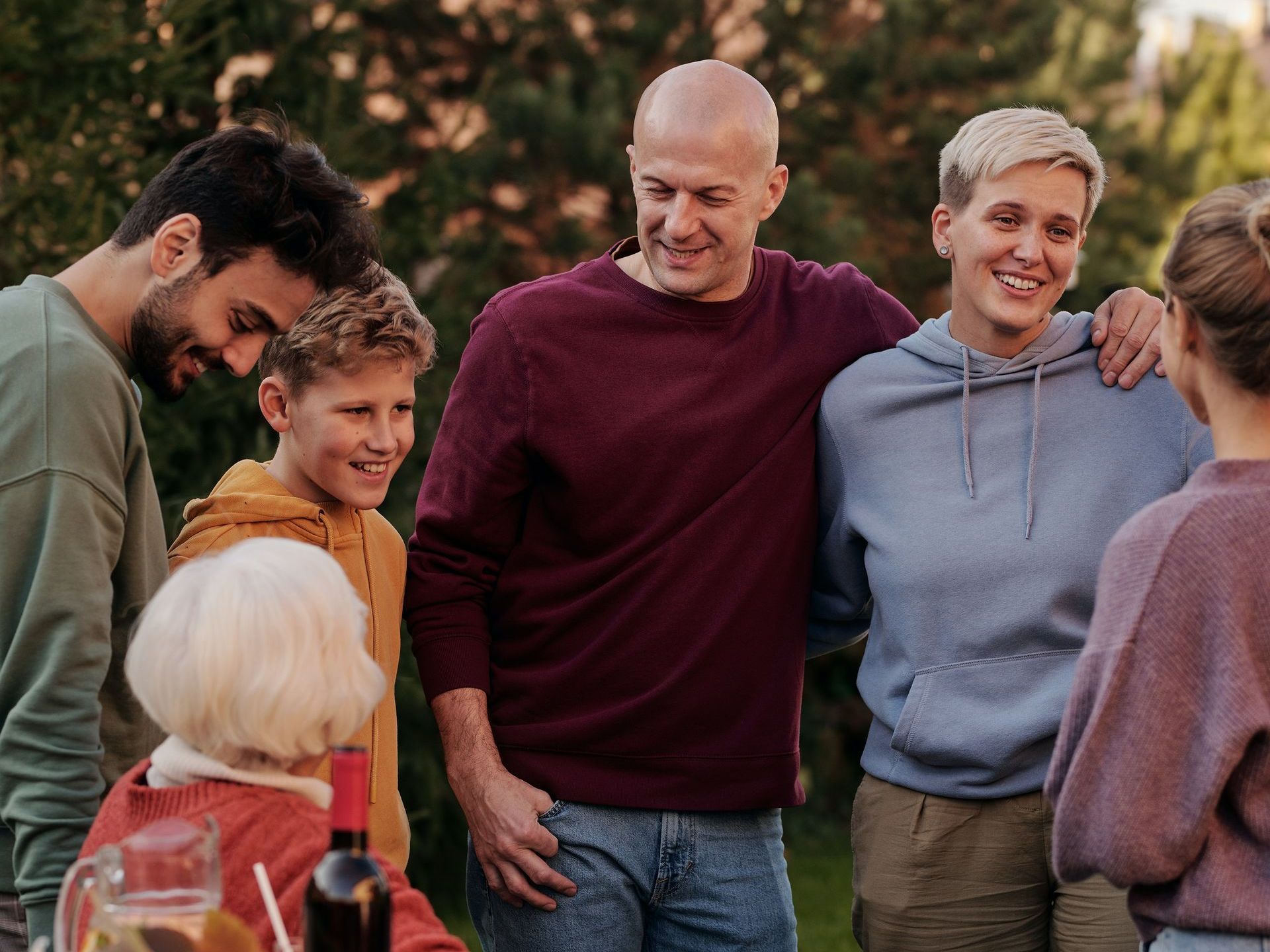 Family gathering outdoors, smiling and embracing. People of various ages in casual clothing.