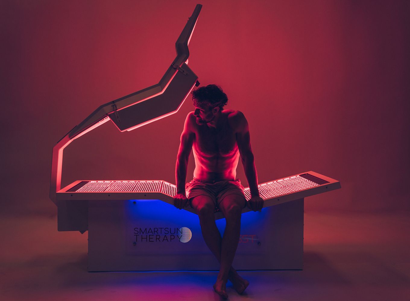 A man is sitting on a bed with red and blue lights on it.