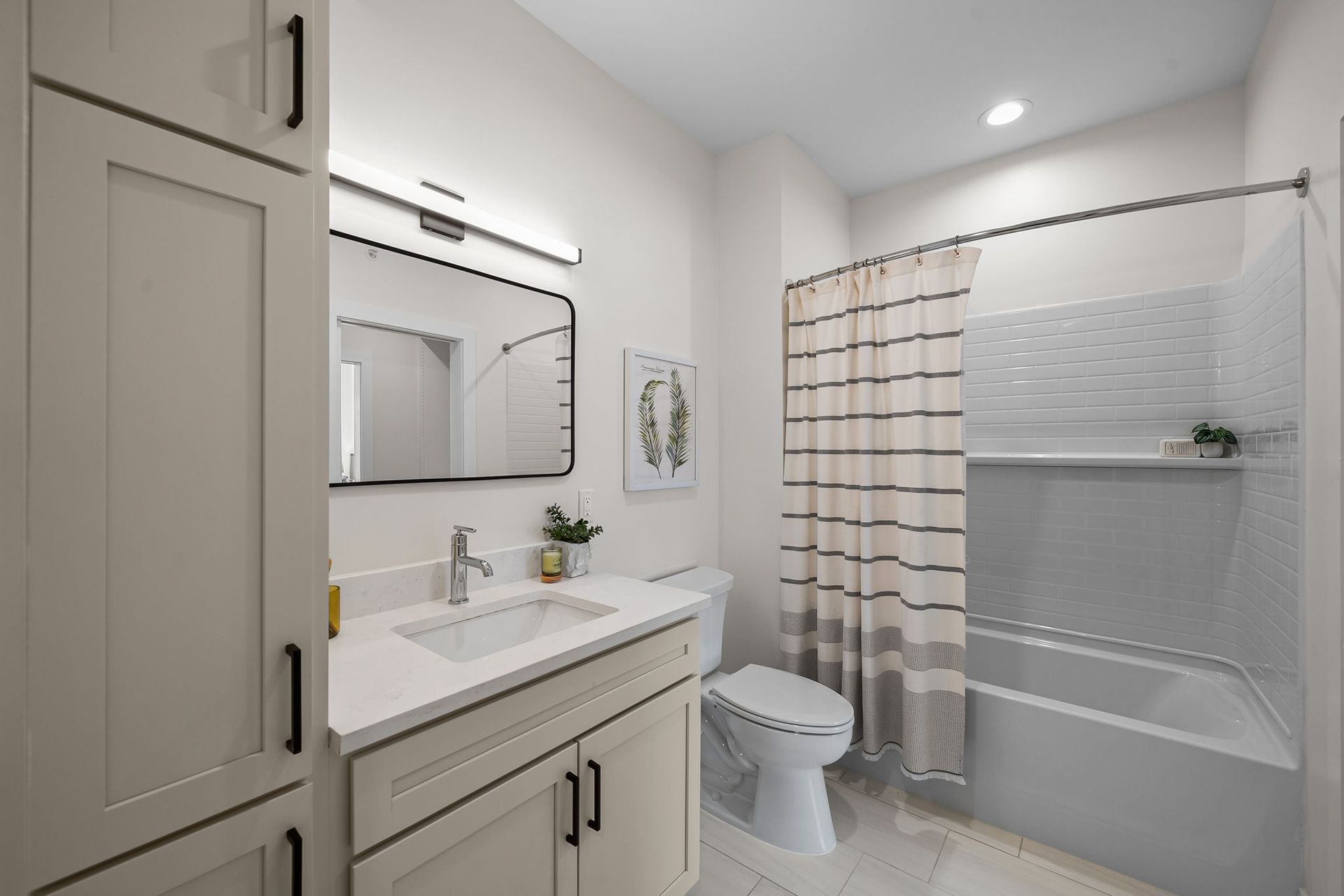 Modern bathroom with vanity, mirror, toilet, bathtub, and gray-striped shower curtain.