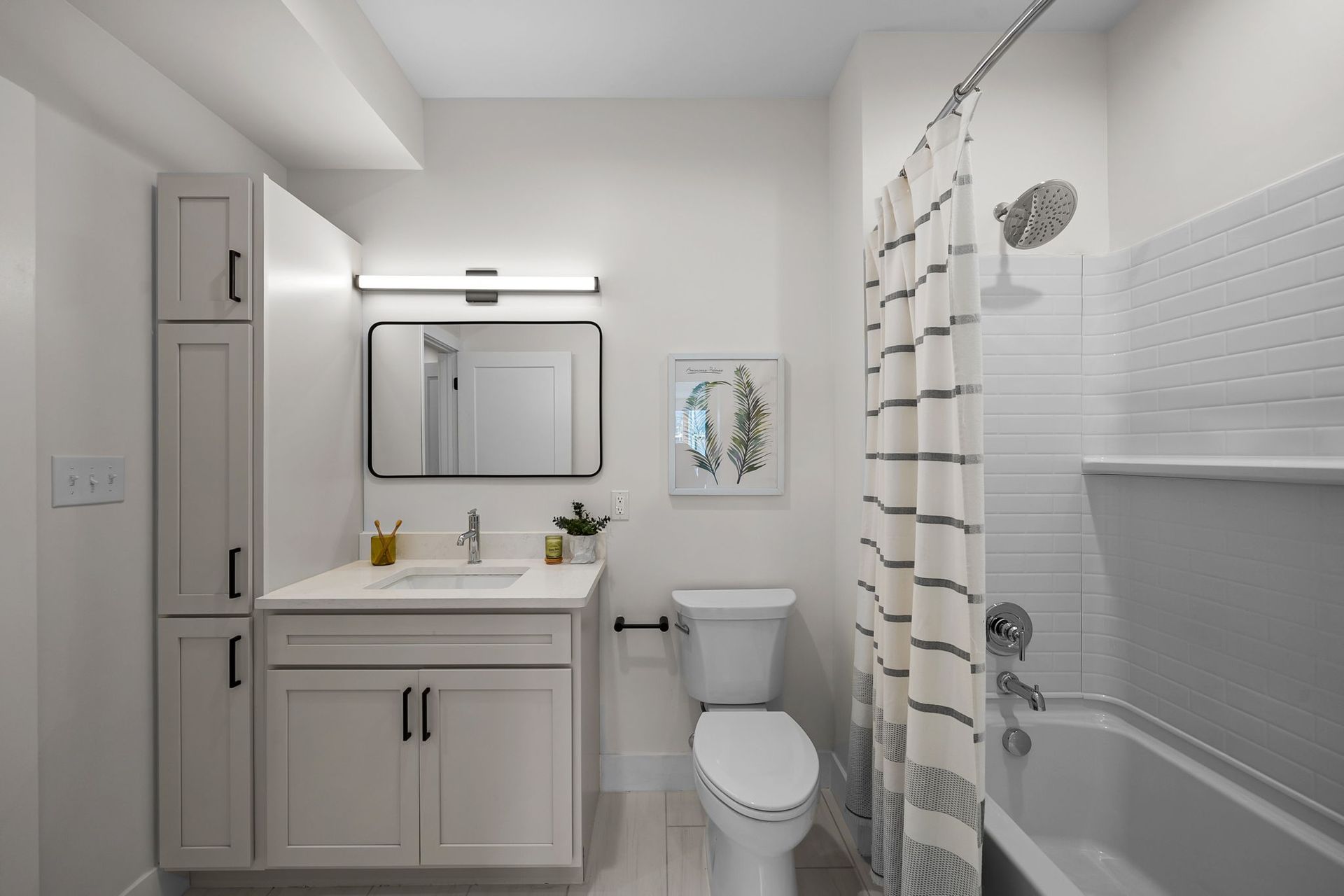 Bright white bathroom with vanity, mirror, toilet, tub, and shower curtain under overhead lights.