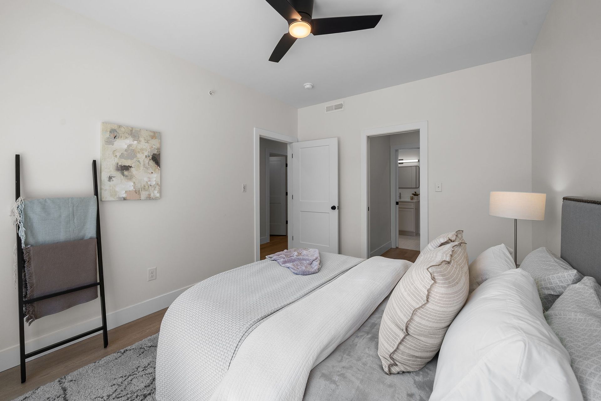 Modern bedroom with gray bedding, ceiling fan, wall art, and a standing mirror