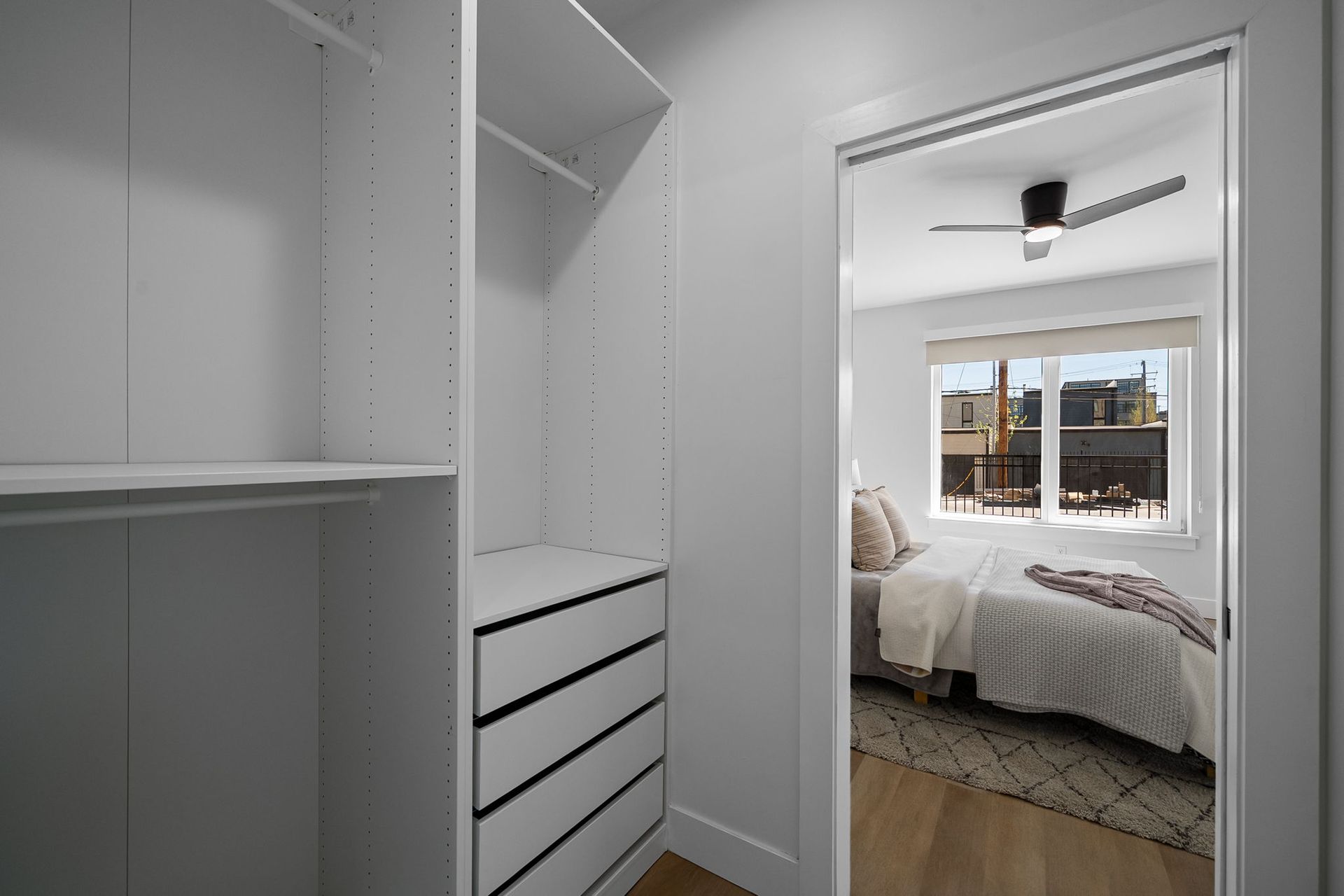 White walk-in closet opening to a bright bedroom with a bed, window, and ceiling fan