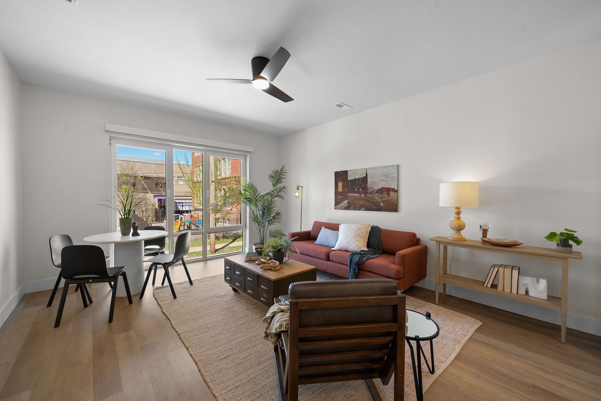 Bright living room with sofa, desk, dining chairs, lamp, and large sliding doors to a balcony