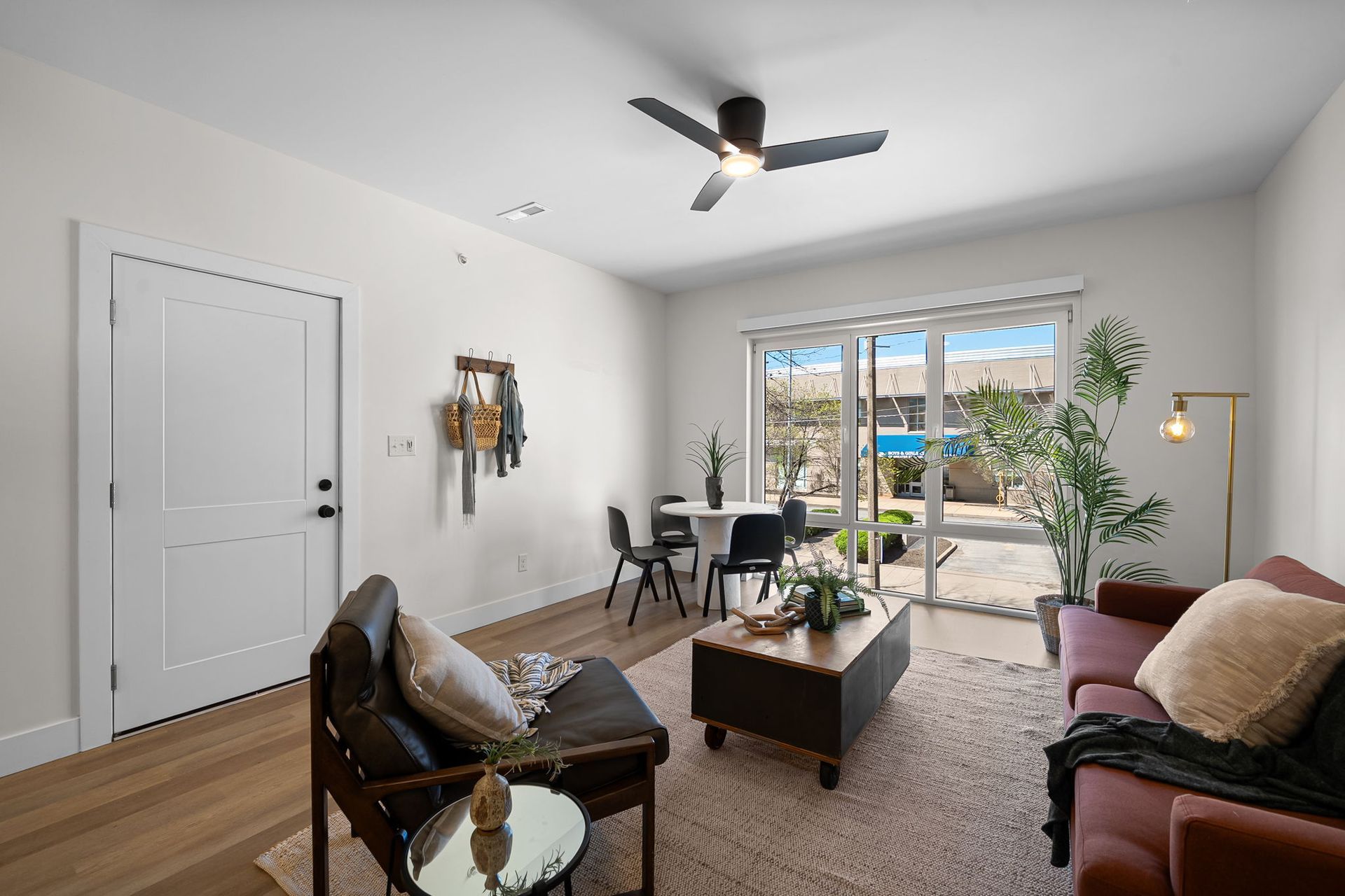Bright living room with sofa, armchair, coffee table, desk, ceiling fan, and balcony view.