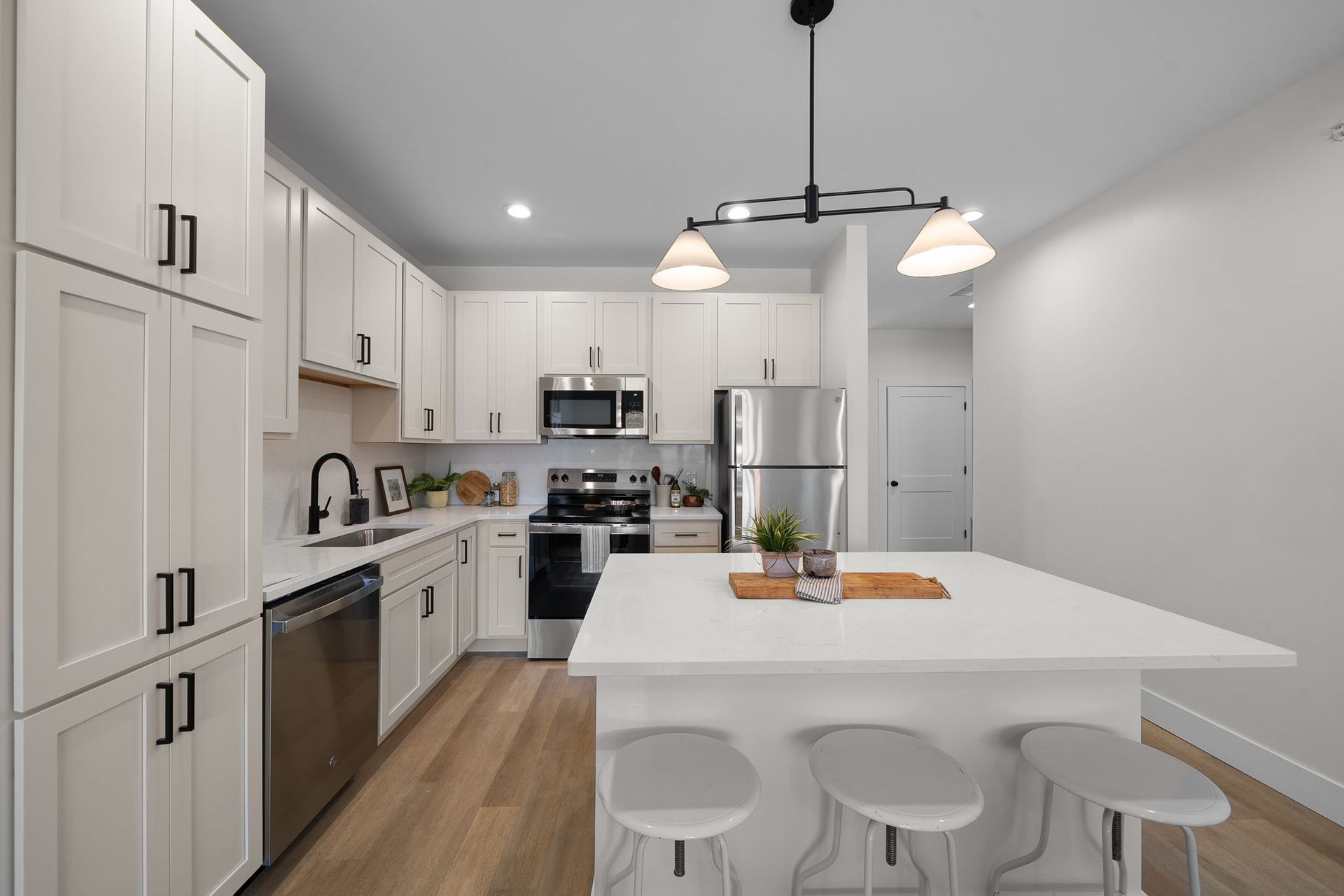 Bright modern white kitchen with island, stools, stainless appliances, and wood floors