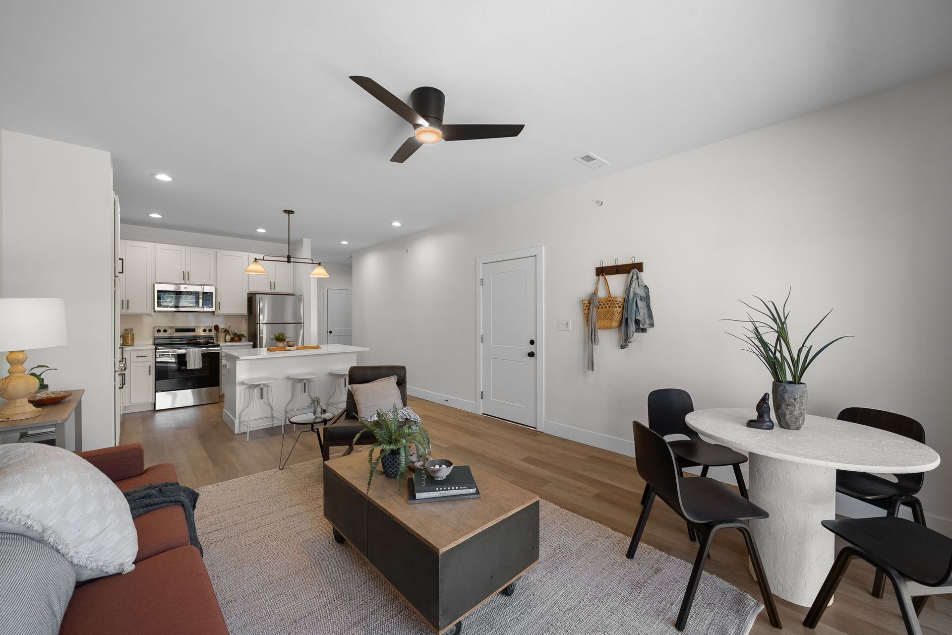 Open-plan living room and kitchen with gray sofa, dining table, and ceiling fan in a bright modern apartment