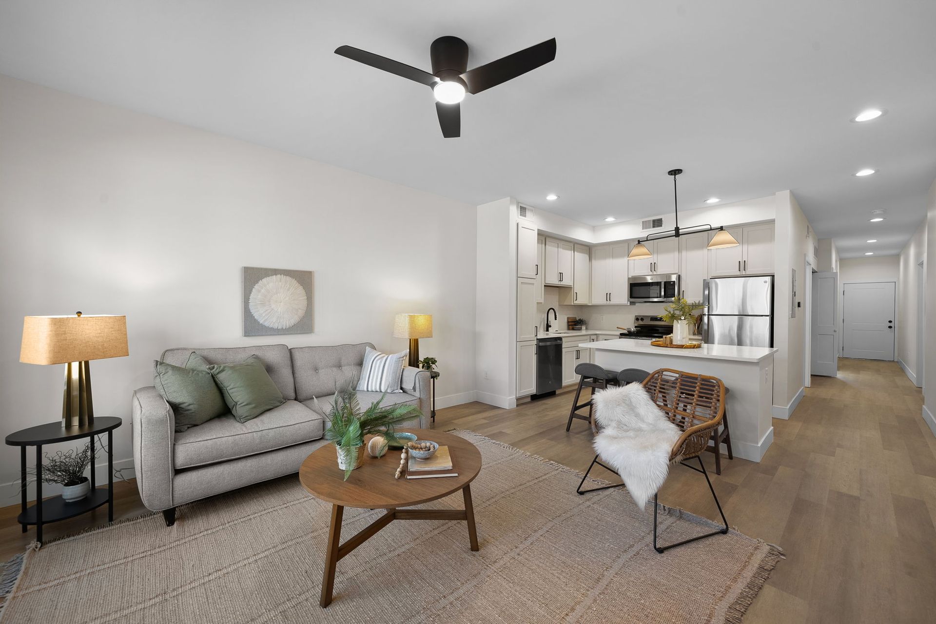 Bright modern living room with gray sofa, wood coffee table, rug, and open kitchen behind it