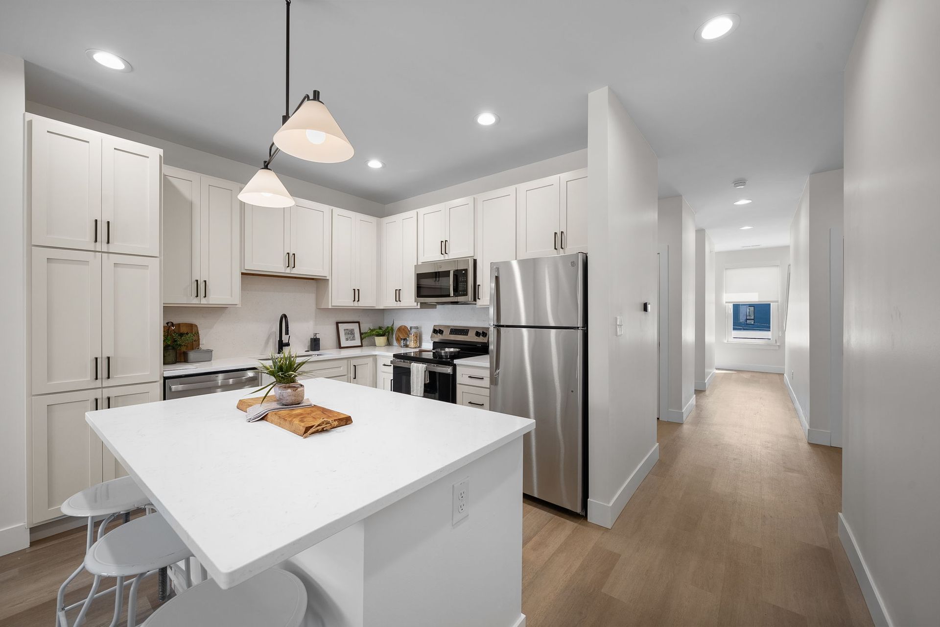 Bright modern kitchen with white cabinets, stainless steel appliances, and a white island under pendant lights