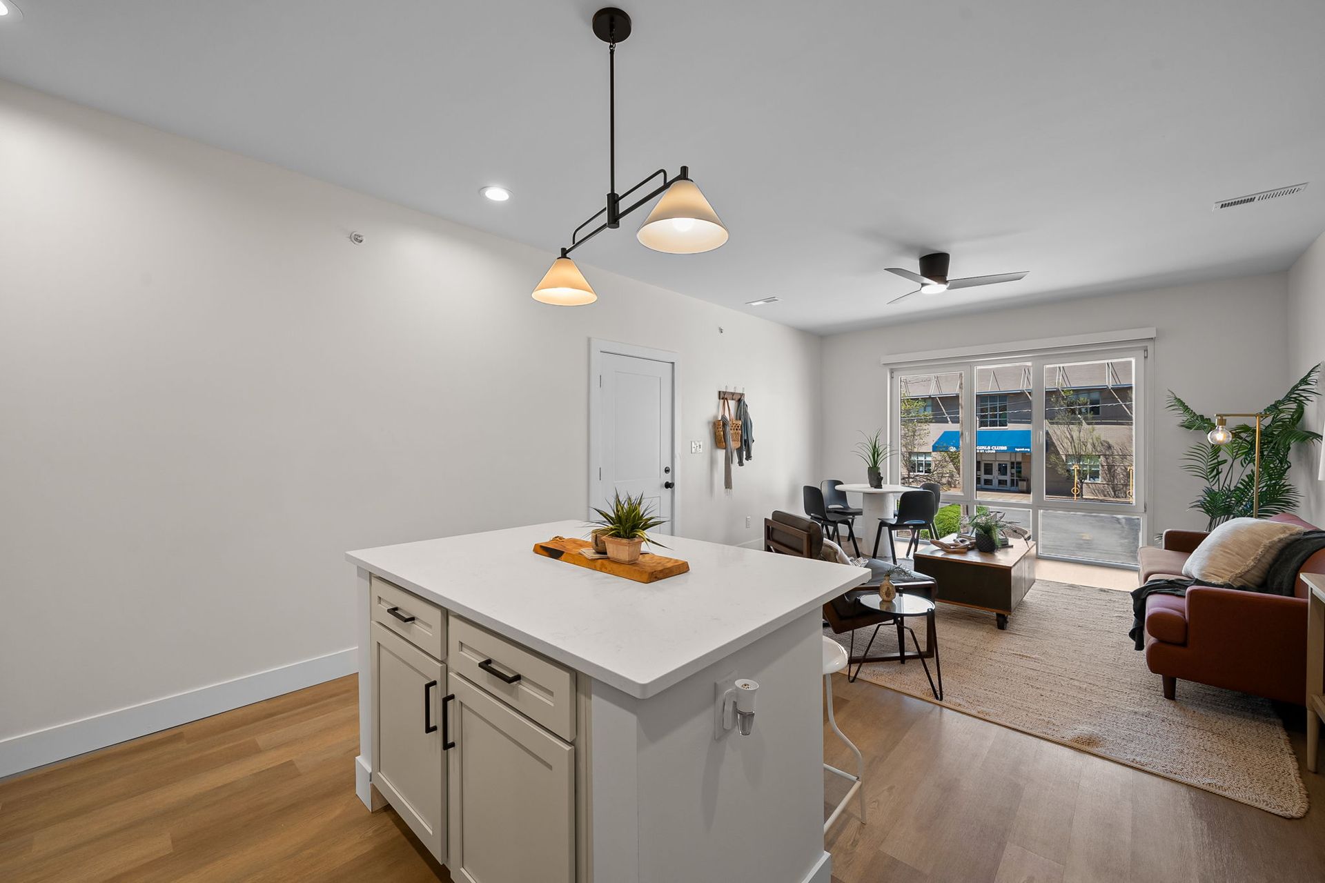 Bright open living room and kitchen with white island, wood floors, and patio doors to a backyard.