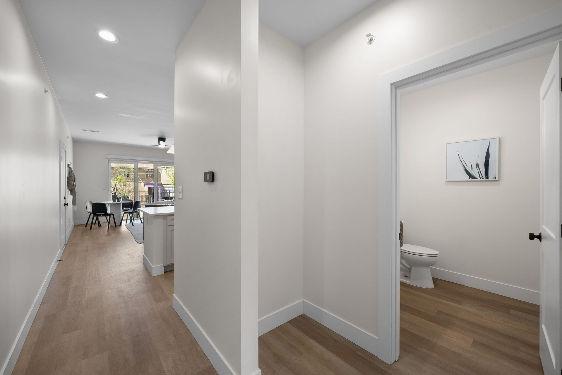 Bright hallway leading to an open kitchen, with a doorway to a small bathroom and wood floors throughout.