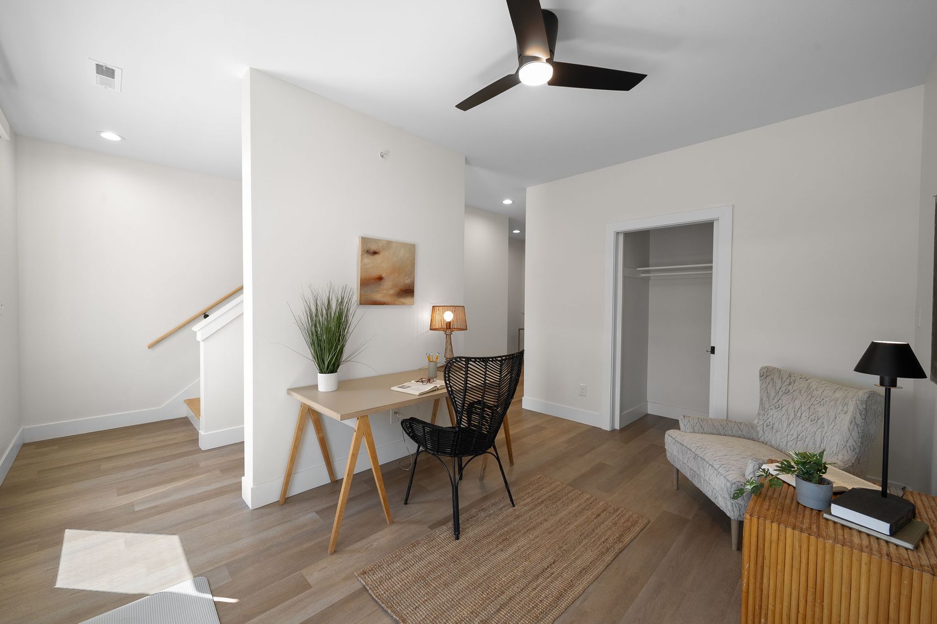 Modern living room with desk, chair, sofa, wood floors, and ceiling fan in a bright white space