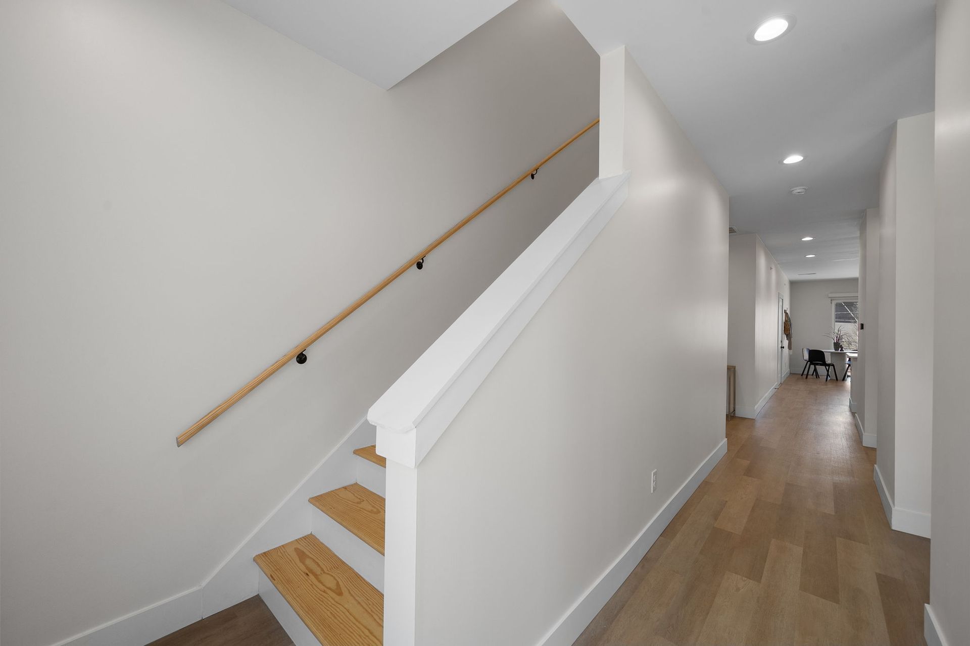 Modern hallway with wood floors and staircase railing leading to an upper floor