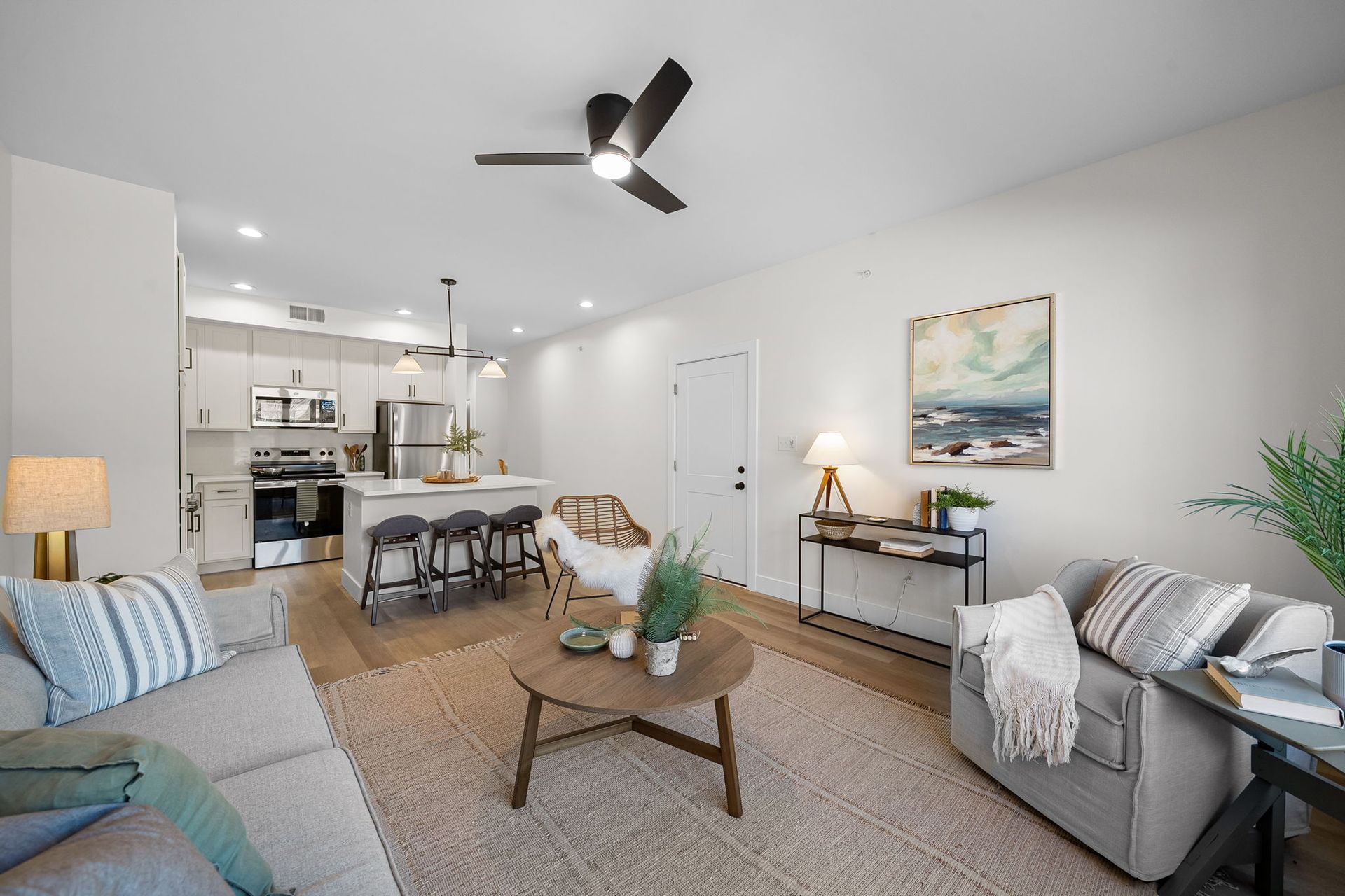 Bright open living room with gray sofas, coffee table, dining area, and kitchen in the background.