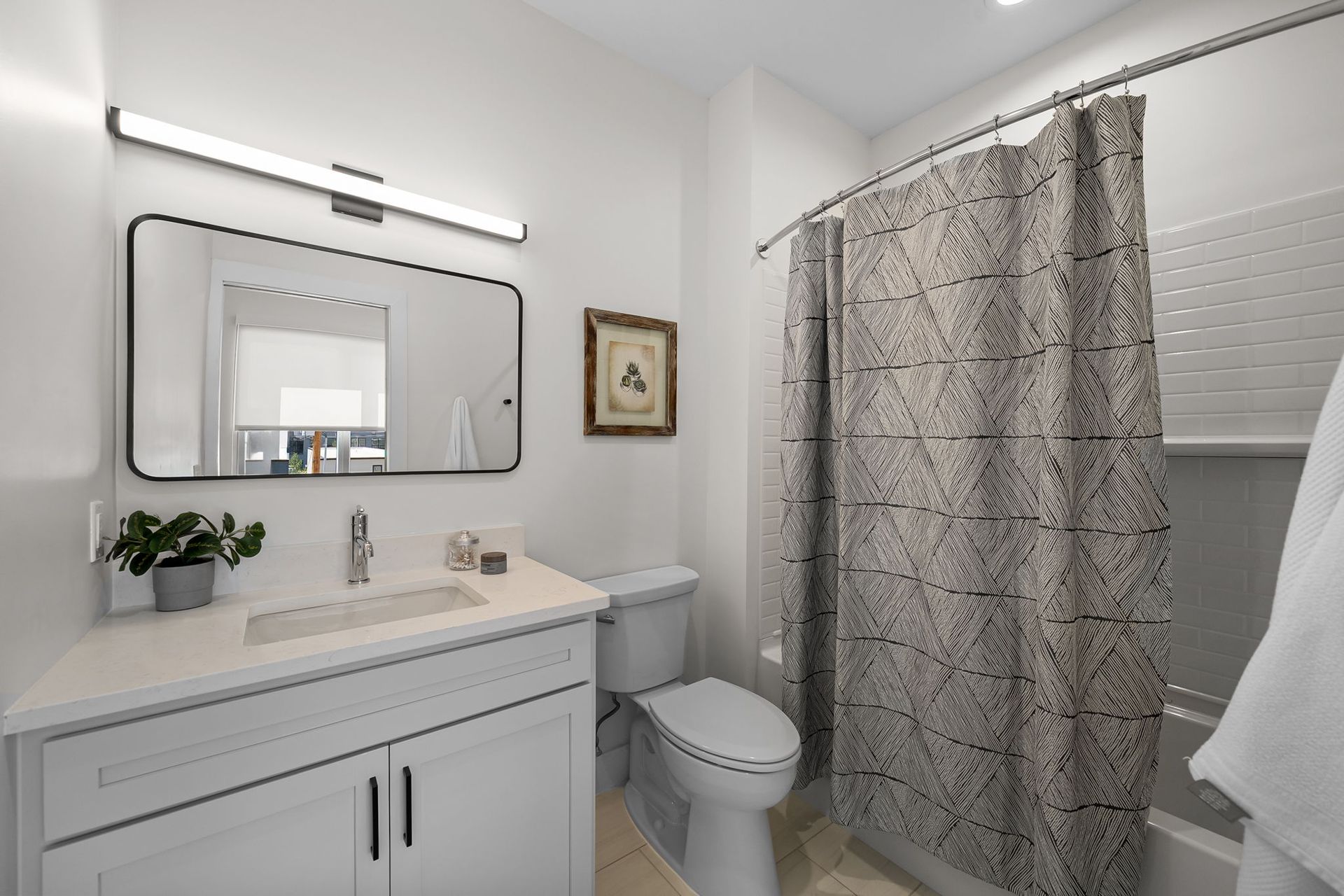 Modern bathroom with white vanity, mirror, toilet, and patterned shower curtain