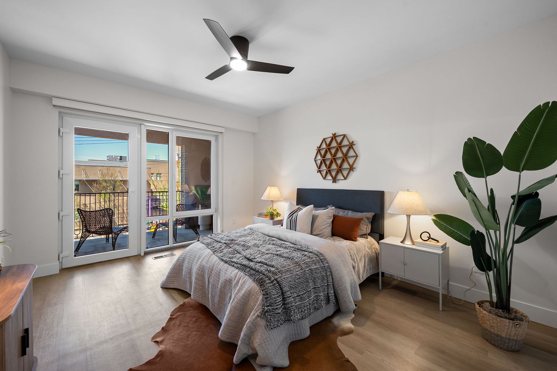 Bright bedroom with a bed, bedside lamps, plants, and French doors to a balcony.