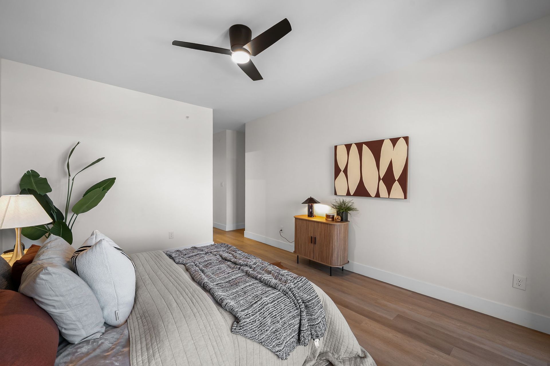 Modern bedroom with a bed, ceiling fan, wood floors, and a dresser with wall art