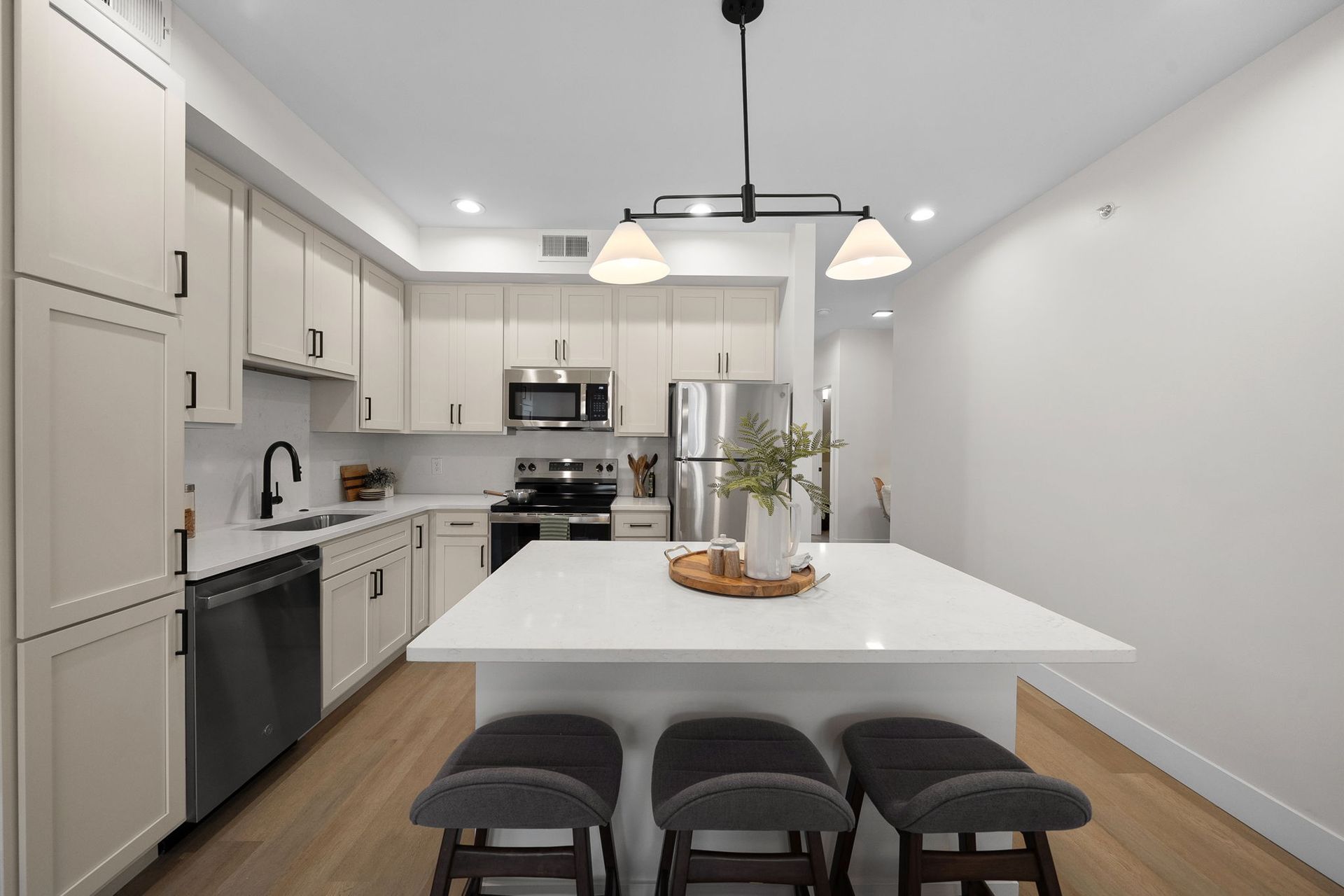 Modern white kitchen with island, black stools, stainless steel appliances, and pendant lights