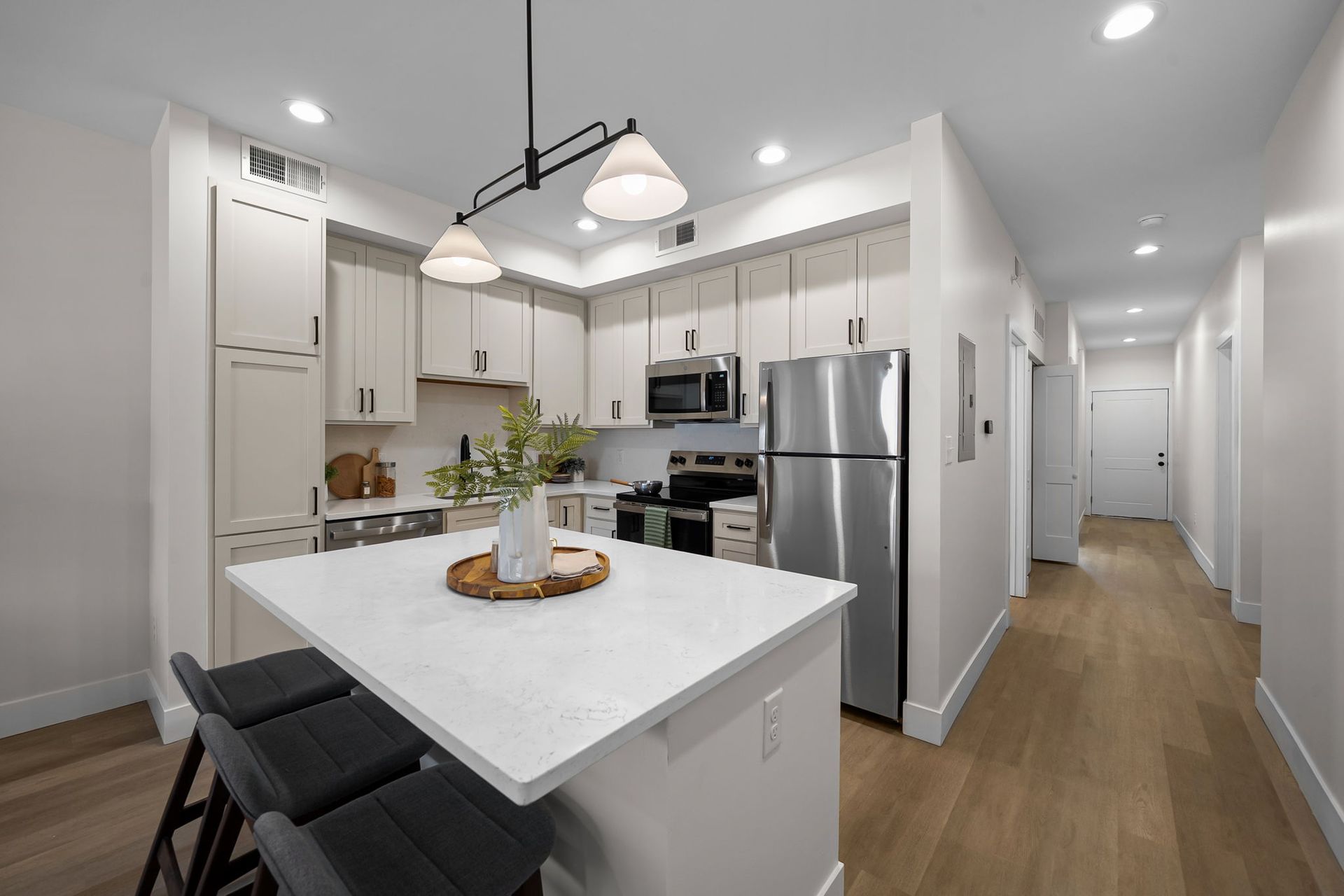 Bright modern kitchen with white cabinets, island seating, and stainless steel appliances leading to a hallway