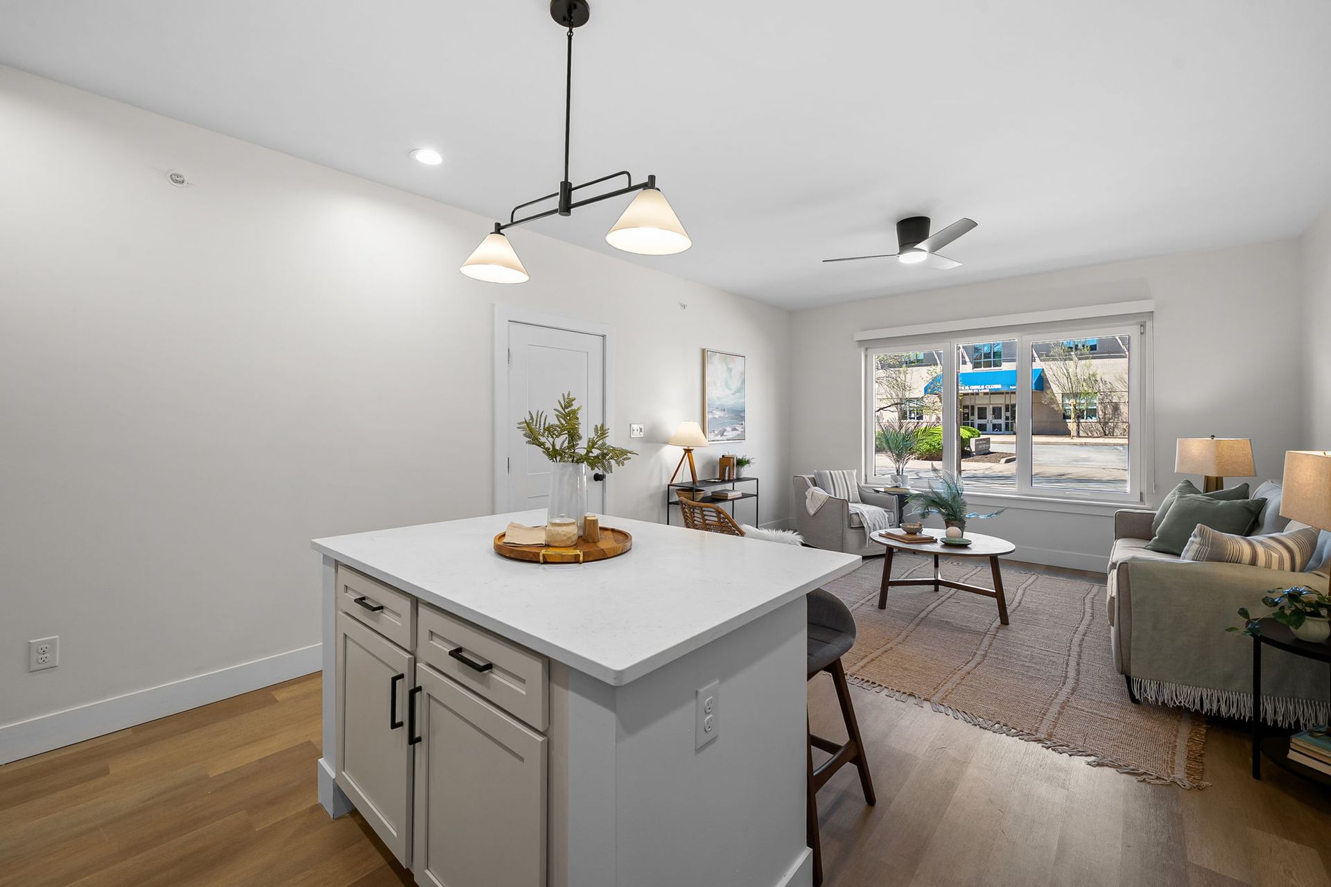 Bright open-plan living room and kitchen with white island, hardwood floors, and large windows.