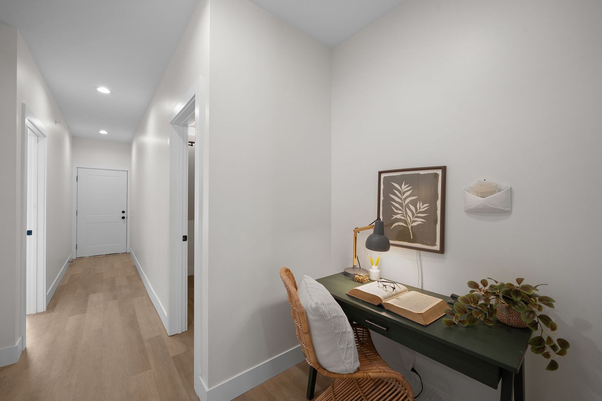 Bright hallway with white walls, wood floors, and a small desk with lamp and plant.