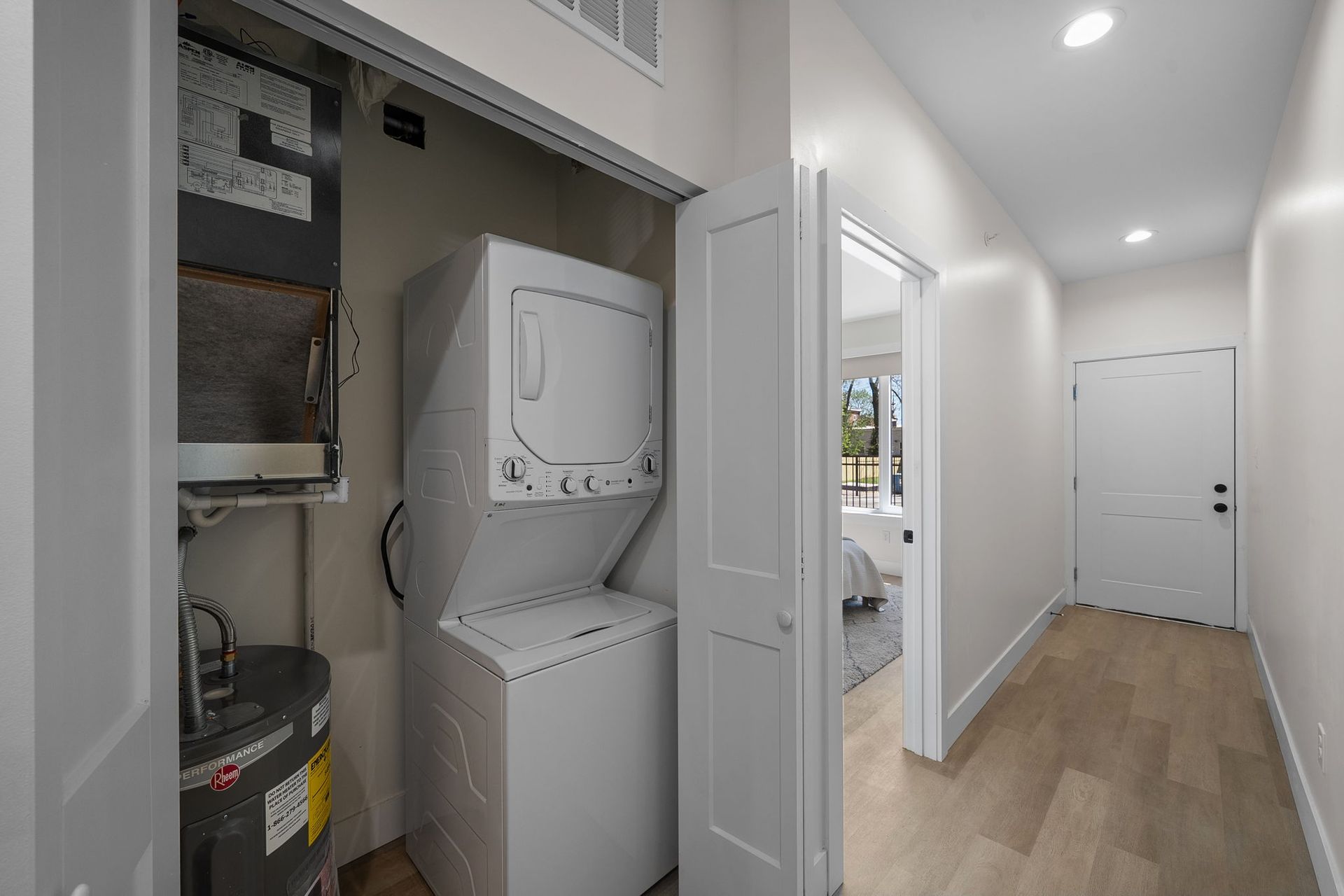 Laundry closet with stacked washer and dryer beside a bright hallway and front door