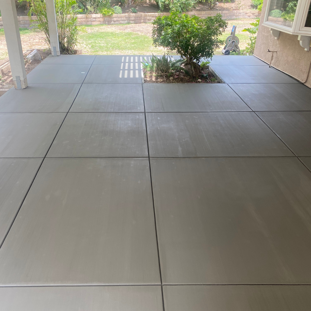 A newly poured, light gray concrete patio with dividing lines and a small tree in the middle.