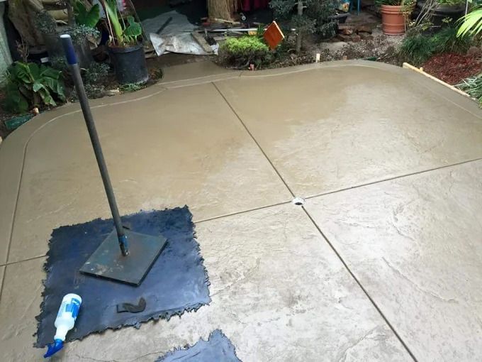 Wet concrete patio with a metal pole on a weighted base and a blue bottle on a mat