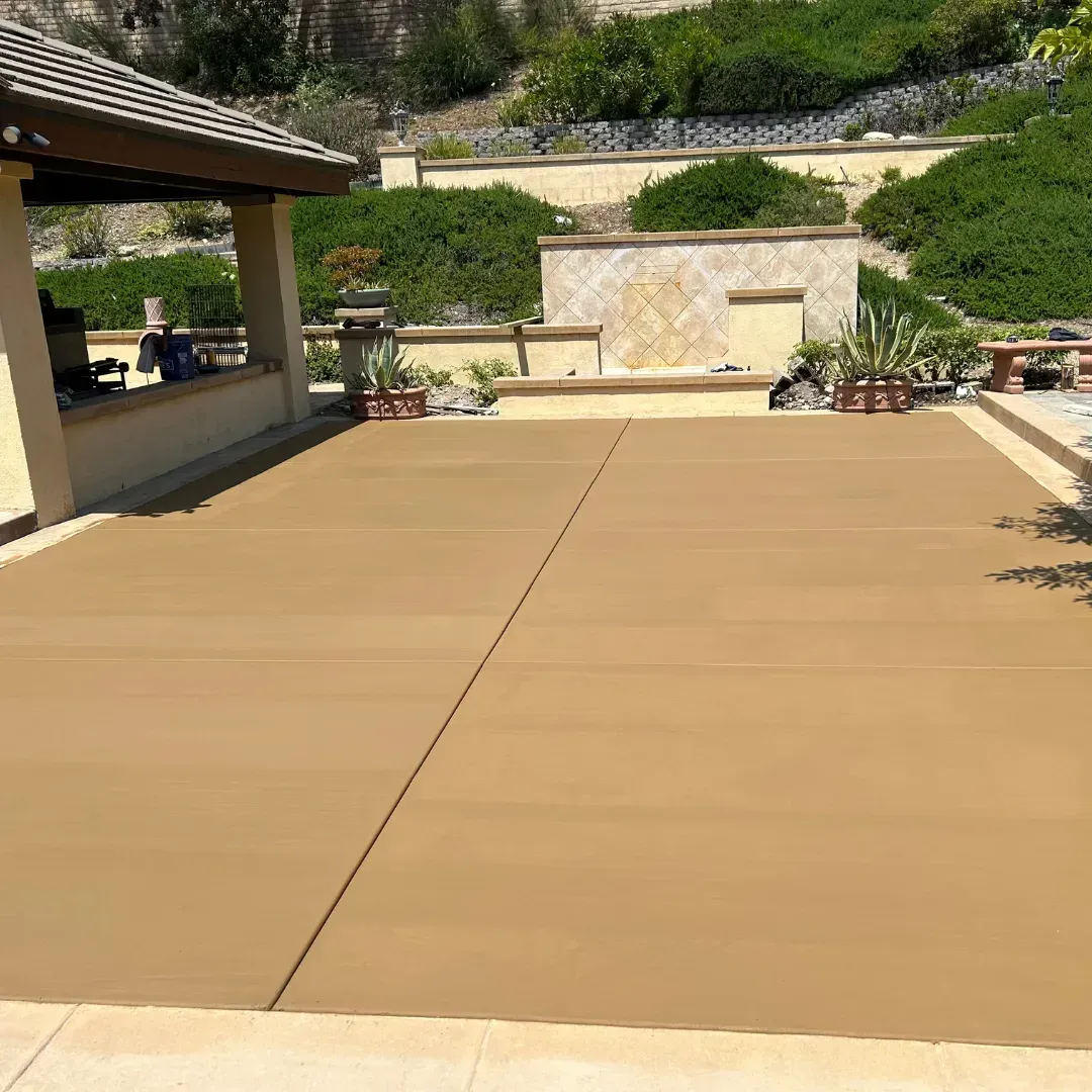 Tan concrete patio with a covered seating area; landscaping in the background.