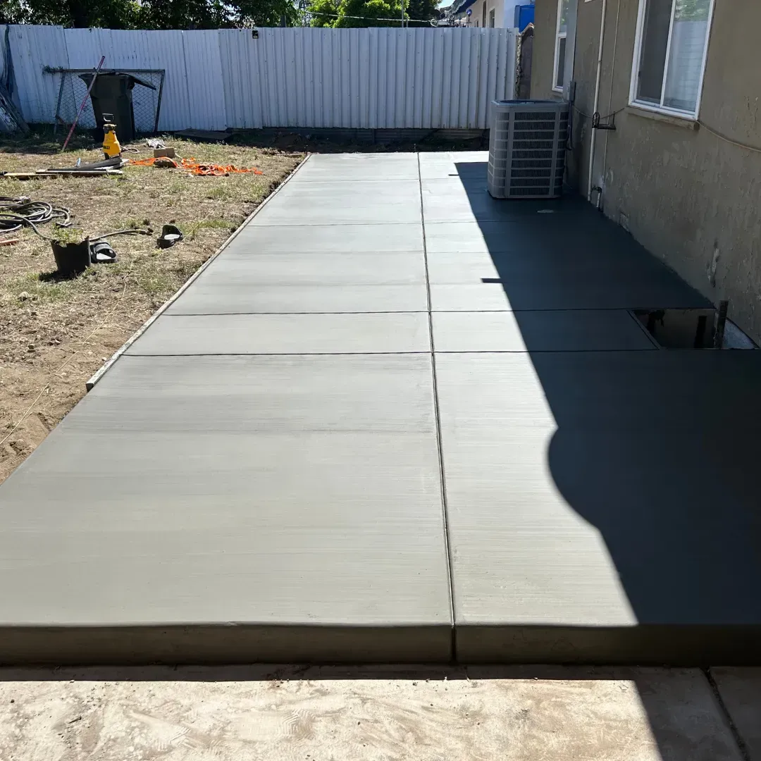 Newly poured concrete patio next to a house with a grass yard.