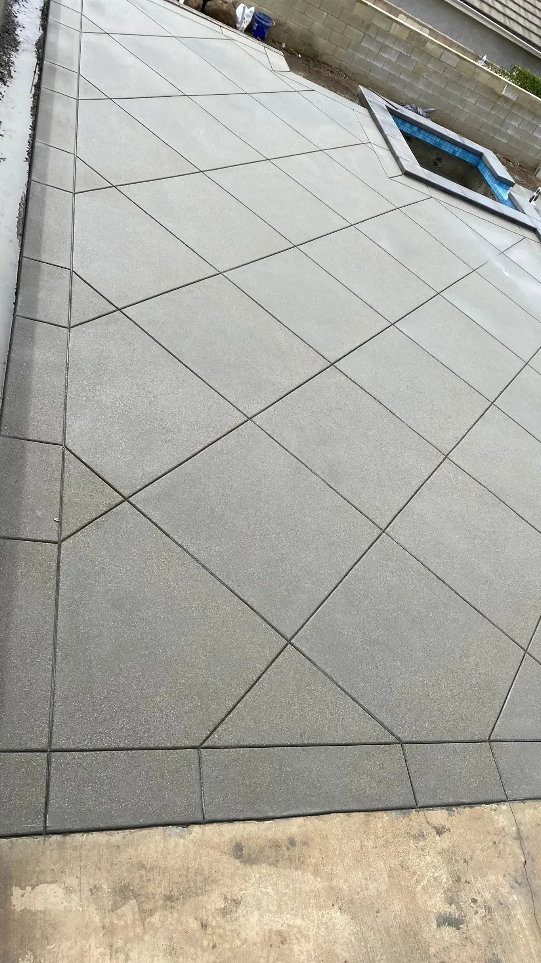 Gray patio pavers arranged in a diagonal pattern, framed by darker border stones, with a small rectangular inset.